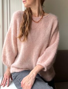 a woman sitting on a bench wearing a pink sweater