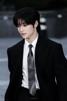 a young man in a suit and tie walking down the street with his hands in his pockets