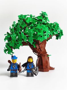 two lego figures standing next to each other under a tree with green leaves on it