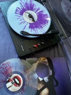 two turntables are sitting next to each other on a bed with purple and white designs