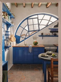 a kitchen with blue cabinets and shelves on the wall, an arched window over the sink