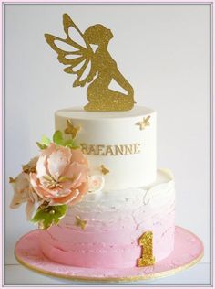 a white and pink cake with a gold fairy topper on it's side