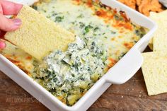 a hand dipping a tortilla chip into a casserole dish with spinach and cheese