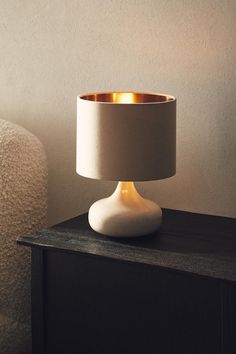 a white table lamp sitting on top of a wooden table next to a chair and wall