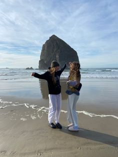 two girls standing on the beach with their arms in the air