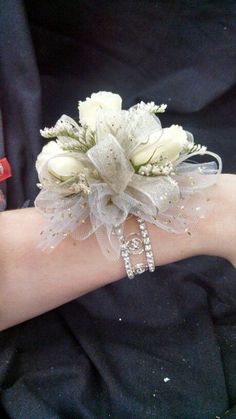 a wrist corsage with white flowers and pearls on it's arm,