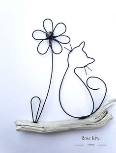 a metal cat sculpture sitting on top of a piece of driftwood with a flower attached to it