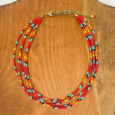 Multilayered seedbeaded choker in red multicolor.  Majority of the beads are red, other colors include; turquoise, black, orange, and yellow. The adjustable  chain has three beads in colors, white, yellow, and  red. These earrings are taken on a brown block. Seed Bead Pendant Necklace, Trendy Red Beaded Necklaces, Red Beaded Necklaces For Summer, Adjustable Red Necklaces For Summer, Red Beaded Choker Necklace For Summer, Summer Red Necklaces With Colorful Beads, Trendy Red Beaded Necklace, Summer Red Necklace With Colorful Beads, Casual Red Beaded Necklace