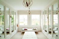 a white room with mirrored doors and a bench in the middle, surrounded by windows