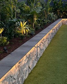 an outdoor garden with grass, plants and stone wall lighting up the side of it