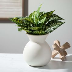 a white vase filled with green plants on top of a table next to a wooden cross