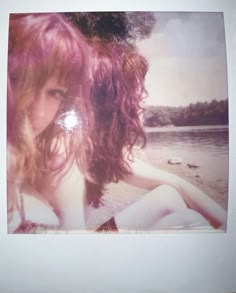 a polaroid photograph of a woman sitting on the beach with her hair blowing in the wind