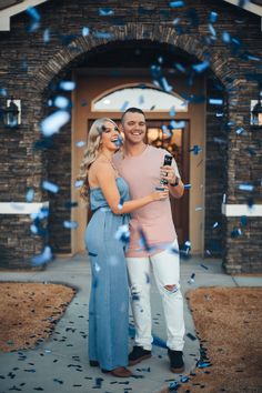 a man and woman standing in front of a house with confetti falling around them