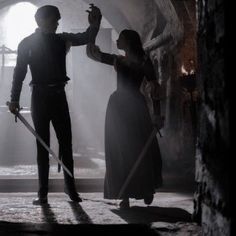 a man and woman standing in a tunnel holding swords with one hand, while the other holds