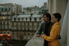 a man and woman standing on top of a balcony looking out at the city below