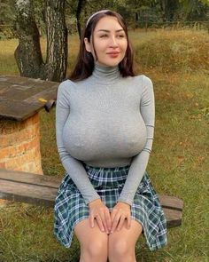 a woman sitting on top of a wooden bench next to a tree and grass covered field