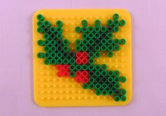 a piece of art made out of legos on a yellow surface with red and green beads