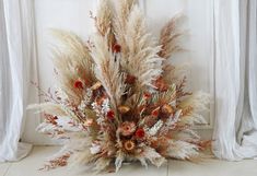 dried flowers and grasses are arranged in a vase on the floor next to a window