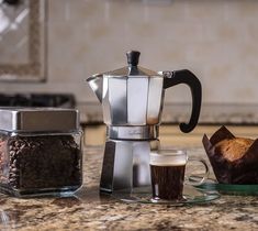 a coffee maker sitting on top of a counter next to two cups and a muffin