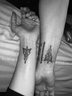 two people with matching tattoos on their arms, both holding each other's hands