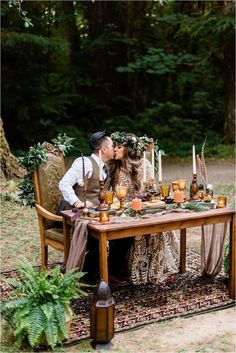 a man and woman kissing at a table with candles on it in the middle of a forest