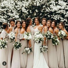 a group of women standing next to each other in front of trees and white flowers