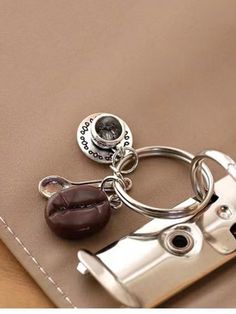 a camera keychain sitting on top of a brown leather bag with a button