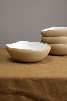 three white bowls sitting on top of a brown cloth covered tablecloth with one bowl in the middle