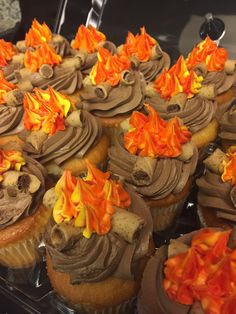 cupcakes with chocolate frosting and orange flames on them in a display case