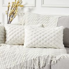 two white pillows sitting on top of a couch next to a vase filled with flowers