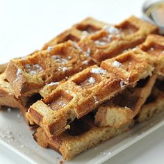 some waffles are stacked on top of each other with syrup and powdered sugar