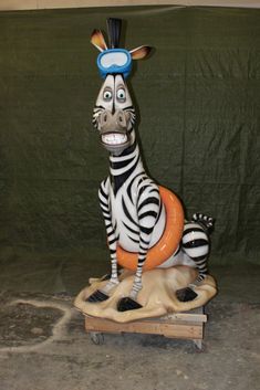 a statue of a zebra sitting on top of a wooden crate with an orange ball in its mouth