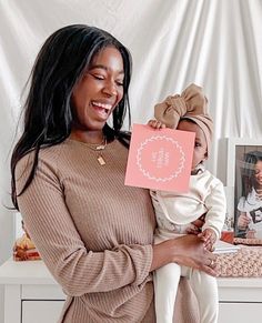 a woman holding a baby in her arms and smiling at the camera while standing next to a table with pictures on it