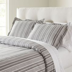 a bed with white sheets and gray striped comforter on top of it in front of a window