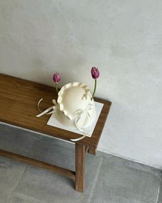 a wooden table with a bowl and two flowers on it, next to a wall