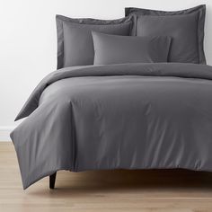 a bed with grey sheets and pillows on top of wooden flooring in front of a white wall