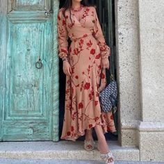 a woman standing in front of an open door wearing a long dress with flowers on it