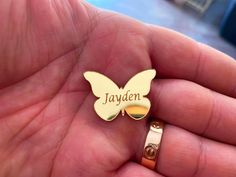 a person holding a gold colored butterfly shaped name pin in their hand with the word jayden written on it