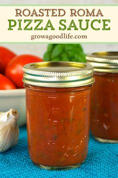 two mason jars filled with roasted tomato pizza sauce on top of a blue towel next to tomatoes and garlic