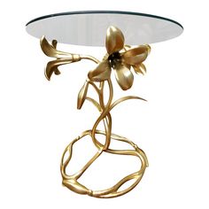 a table with a glass top and gold metal flowers on the base, against a white background