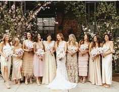 a group of women standing next to each other in front of flowers and bushes on the sidewalk