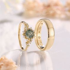 two gold wedding rings with green and white diamonds on top of each other, sitting next to seashells