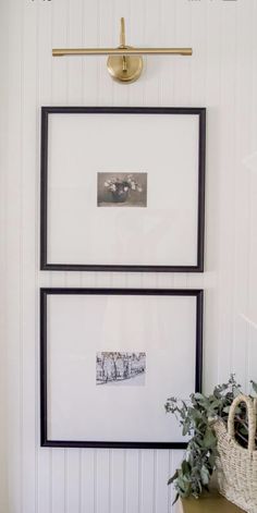 two framed pictures hang on the wall above a table with a basket and potted plant