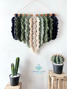 there is a wall hanging made out of yarn and some cactuses on the table