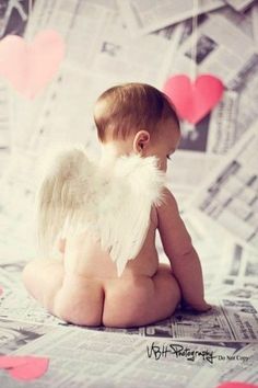 a baby with angel wings sitting on top of a bed next to paper heart shapes