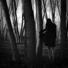 black and white photograph of a woman standing in the woods with her back to the camera