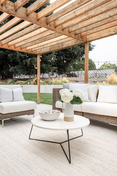 an outdoor living area with white furniture and wood pergolated roof over the patio