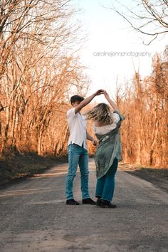 two people standing in the middle of an empty road with bare trees behind them and one person holding his arm up