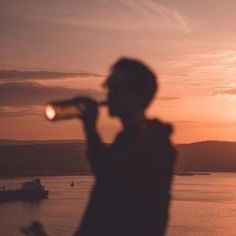 a man is drinking from a bottle at sunset