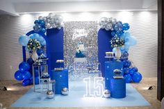 a blue and silver birthday party with balloons, cake and decorations on the stage for an event